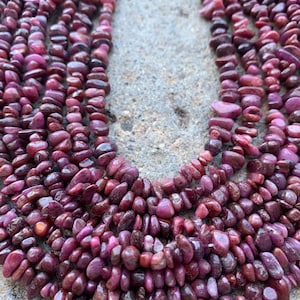 May include: A strand of ruby gemstone beads, featuring a deep red color and a chip-shaped design. The beads are arranged in a loose, flowing pattern, creating a natural and organic look.