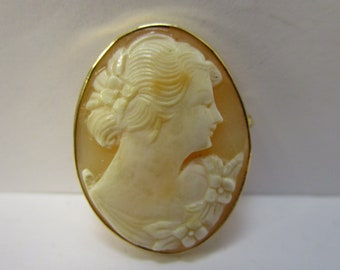 Puede incluir: Un broche de camafeo dorado con un camafeo de concha tallada de un perfil de mujer con detalles florales.