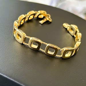 May include: A gold bracelet with a chain link design featuring square-shaped links. The bracelet has a clasp closure.