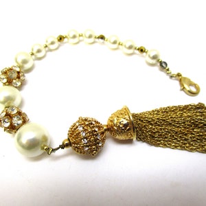 May include: A gold bracelet with a tassel charm and faux pearl and rhinestone beads.