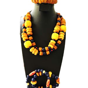 Puede incluir: Un conjunto de joyas que incluye un collar, una pulsera y una pulsera de puño. El collar y la pulsera tienen cuentas amarillas y azules. La pulsera de puño está hecha de cuentas de color ámbar. Las joyas se exhiben en un maniquí negro.