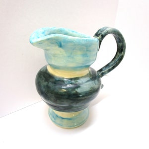 Könnte beinhalten: Eine Keramikkanne mit blauer, weißer und grüner Glasur. Die Kanne hat einen breiten, runden Körper und einen Henkel.