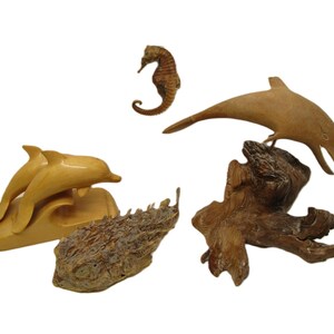以下が含まれることがあります： タツノオトシゴ、イルカ2匹、流木など、海の生き物をモチーフにした木製置物のセット。置物は明るい茶色の木で彫られており、自然な仕上げになっています。