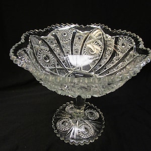 Könnte beinhalten: Eine klare Glasschale auf einem Sockel mit einem gewellten Rand und einem komplizierten geschliffenen Glasdesign. Die Schale steht auf einem Sockel mit einem runden Fuß.