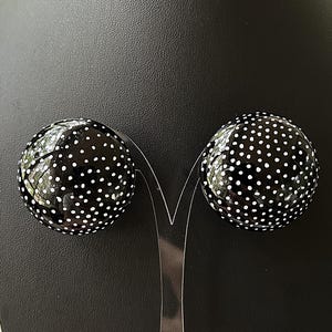 May include: A pair of black and white polka dot earrings. The earrings are round and have a glossy finish.
