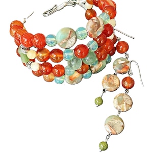 Puede incluir: Un conjunto de joyas hecho a mano con un brazalete y aretes a juego. El brazalete está hecho de cuentas naranjas, verdes y azules. Los aretes tienen un diseño en cascada con cuentas similares y ganchos plateados.