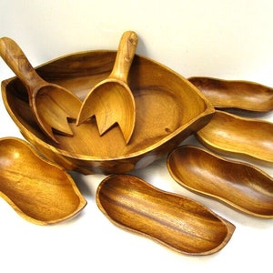 Pode incluir: Um conjunto de tigelas de servir e colheres de salada de madeira. O conjunto inclui uma tigela grande em forma de folha, quatro tigelas menores e duas colheres de servir. As tigelas são todas feitas de madeira natural e têm um visual quente e rústico.