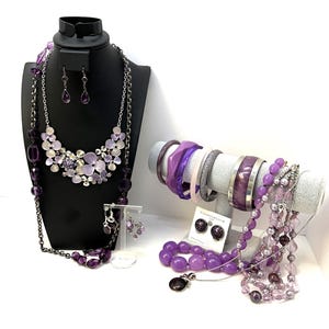 May include: A set of purple jewelry including necklaces, bracelets, earrings, and a pendant. The jewelry is made of beads, metal, and plastic.