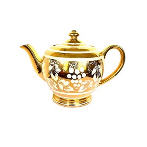 May include: A gold teapot with a white grape design. The teapot has a round body and a spout on the side. The handle is on the opposite side of the spout.