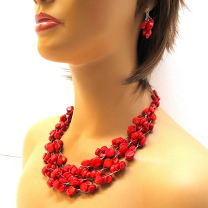 May include: A multi-strand necklace and matching earrings made of red coral beads. The necklace is made of several strands of coral beads that are connected by a thin wire. The earrings are made of a cluster of coral beads.