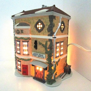 May include: A ceramic light-up model of a post office building with a red door and a sign that reads "King's Road Post Office". The building has a brown roof and a brick facade with green vines growing up the side.