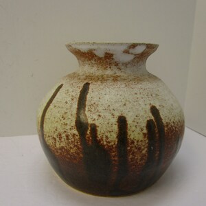 Peut inclure: Un vase en céramique blanche avec un glaçage brun et jaune. Le vase a un corps arrondi et un col étroit.