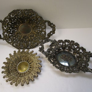 May include: Three ornate metal serving dishes with decorative filigree designs. The dishes are made of a gold-toned metal and have a mirrored finish.