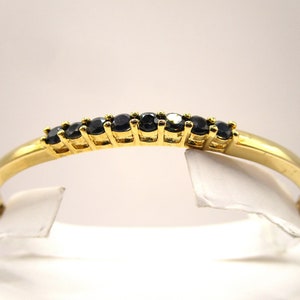 May include: A gold bangle bracelet with a row of black gemstones.