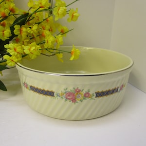 May include: A white ceramic baking dish with a floral design and a silver rim. The dish has a swirl pattern and is decorated with pink, yellow, and blue flowers.