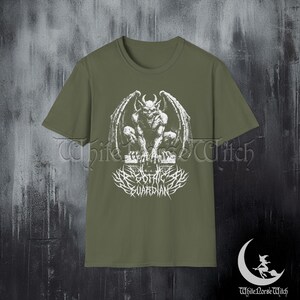 May include: Olive green t-shirt featuring a white graphic of a gargoyle with spread wings, perched atop a stone structure. Below the gargoyle is the text "Gothic Guardian" in a stylized font. The shirt has a crew neck and short sleeves.
