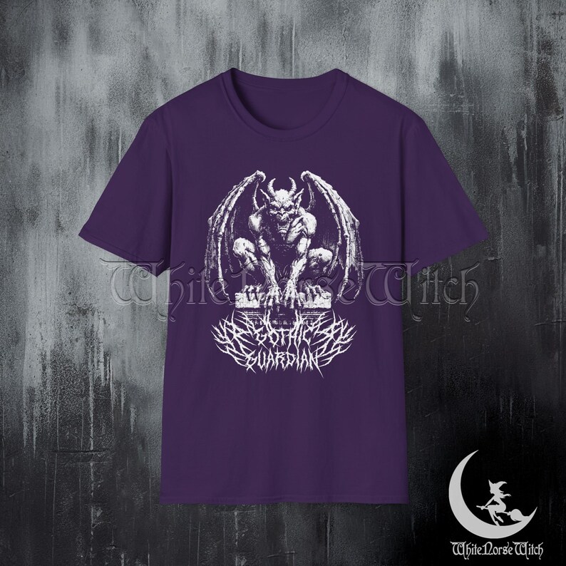 May include: A purple t-shirt featuring a detailed white graphic of a gargoyle with large wings, perched on a stone structure. Below the gargoyle is the text "Black Gothic Guardian" in a stylized font. The shirt has a crew neck.