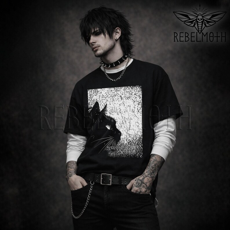 May include: A black short-sleeved t-shirt layered over a white long-sleeved shirt. The t-shirt features a graphic print of a black cat in profile against a textured white background. The text REBELMOTH is visible in the top right corner.