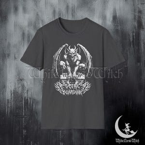 May include: Dark gray t-shirt featuring a detailed white illustration of a gargoyle with large wings, perched on a stone structure. Below the gargoyle is the text "DARK GOTHIC GUARDIAN" in a stylized font. The shirt has short sleeves.