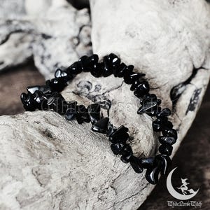 Könnte beinhalten: Armband aus schwarzen Edelstein-Chips aus schwarzem Obsidian. Das Armband besteht aus kleinen, unregelmäßig geformten Chips aus schwarzem Obsidian, die auf einer durchsichtigen elastischen Schnur aufgefädelt sind.