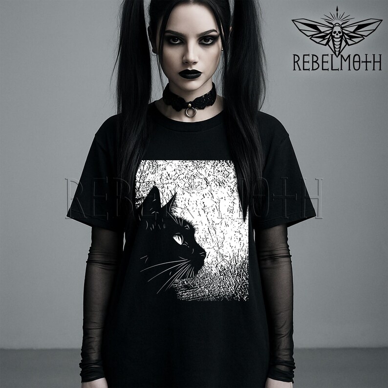 May include: A black t-shirt featuring a graphic print of a black cat in profile against a textured white background. The shirt includes a black choker with a metal ring and sheer black long sleeves. The text REBELMOTH appears in the upper right.