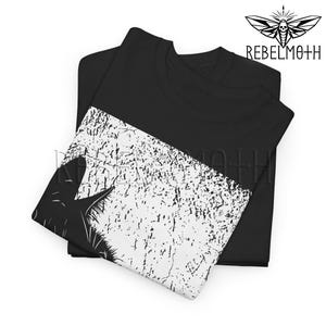 May include: A black t-shirt featuring a graphic print with a white, distressed, textured diagonal section. The print includes a black silhouette of a cat's head and ears. The text REBELMOTH is printed in black above the graphic design.