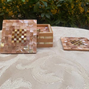 May include: A set of square coasters with a matching box. The coasters and box lid are covered in a mosaic of iridescent, light brown, and gold squares. The center of each coaster features a checkerboard pattern.