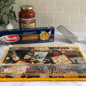 May include: A glass baking dish with a patterned fabric hot pad underneath. The dish is empty and ready for use. A box of spaghetti and a jar of pasta sauce are in the background.