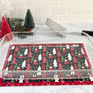 May include: A clear glass baking dish with a red and white Christmas tree patterned fabric liner. The liner has a black background with white snowflakes and green trees.