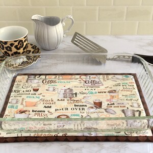 May include: A glass baking dish sits on a brown and beige coffee-themed kitchen mat. The mat features a variety of coffee-related illustrations and text, including "I love coffee", "Nitro Cold Brew", "Add Whipped Cream", and "Pour Over".