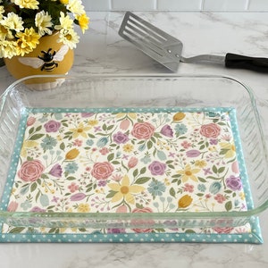 May include: A glass baking dish with a floral patterned fabric liner. The liner has a light blue border with white polka dots.