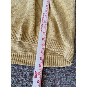 May include: Close-up of a mustard yellow sweater with a ribbed hem. A measuring tape is placed vertically across the sweater, showing measurements from 19 to 32 inches. The text "The helpful place" is printed on the tape.