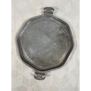 May include: A metallic gray, octagonal serving tray with a smooth, flat center and a raised rim. The tray features two symmetrical, stylized handles extending from opposite sides, each with a distinct notched design at the outer edge.