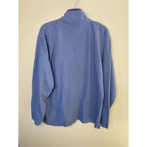 May include: A long-sleeved, light blue pullover shirt with a textured, ribbed fabric pattern. The garment features a high collar with a partial zipper closure at the neck, long sleeves, and a straight hemline, presented from a back-facing view.
