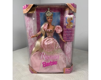 May include: A Rapunzel Barbie doll in a pink satin gown with gold trim, wearing a gold crown and long blonde hair. The doll is inside a rectangular box with purple and pink marble-patterned sides and the text Let my hair down from my crown again n again.