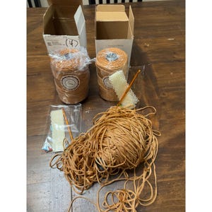 May include: A wooden table displays craft supplies. Two spools of orange-brown yarn are in boxes, alongside a ball of loose yarn and a crochet hook. A small package contains a crochet project.