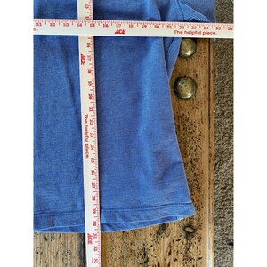 May include: A blue ribbed long-sleeve shirt featuring a horizontal and vertical Ace measuring tape. The horizontal tape shows a width of approximately 12 inches, while the vertical tape indicates a length of approximately 18 inches.