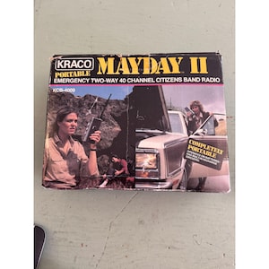 Puede incluir: Una caja de cartón rectangular para una radio portátil de emergencia bidireccional de 40 canales Kraco Mayday II, modelo KCB-4009. La caja presenta texto amarillo y blanco sobre fondo negro, con imágenes de la radio en uso.