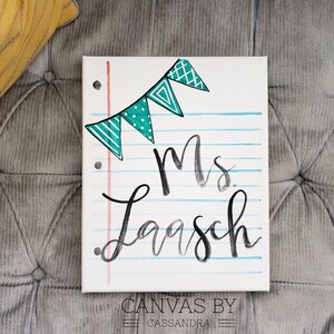 May include: A white canvas with a blue and green patterned banner at the top. The canvas has a red and white lined background with the text "Mrs. Laasch" written in black.