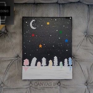 May include: A black canvas painting with a night sky scene. The painting features a crescent moon, stars, and a row of white trees with colorful accents. The bottom of the painting is white, representing snow. The painting is signed "Canvas by Cassandra".