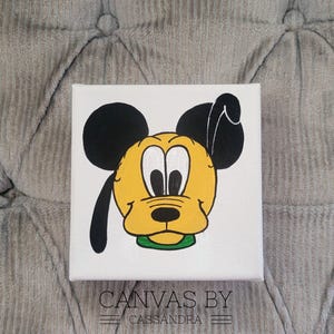 May include: A hand-painted canvas featuring a cartoon illustration of Pluto, the Disney dog. Pluto is depicted with his signature yellow fur, black ears, and a green collar. The canvas is white with the text "CANVAS BY CASSANDRA" at the bottom.