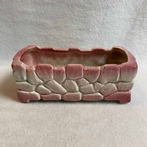 May include: A rectangular ceramic planter with a stone-like design. The planter is pink and white with a textured surface.