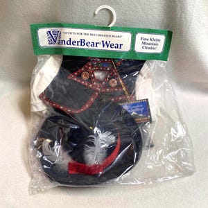 Op de afbeelding: Een verpakt berenoutfit van WanderBear Wear. De outfit bevat een zwart vest met rode en gouden afwerking, een bijpassende hoed met een rode band en witte veren en een wit overhemd. De verpakking leest "Outfits for the Best-Dressed Bears."