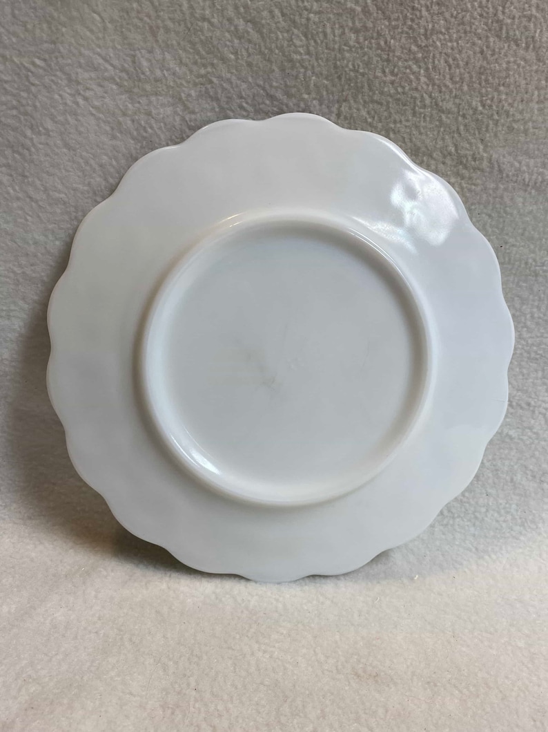 May include: White milk glass plate with a scalloped edge. The plate is plain and has no design.