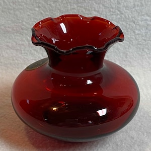May include: A small, round, red glass vase with a scalloped rim.