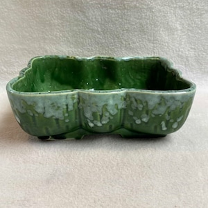 May include: A green ceramic planter with a wavy rim and a mottled glaze. The planter has a square shape with rounded corners and a slightly raised base.