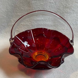 May include: A red glass bowl with a clear glass handle. The bowl has a ruffled edge and a slightly amber-coloured bottom.