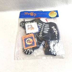 May include: A black Halloween skeleton costume with white bone detailing, packaged in a clear plastic bag. The costume is from "The Muffy Collection" and includes a small "Trick or Treat" tag.