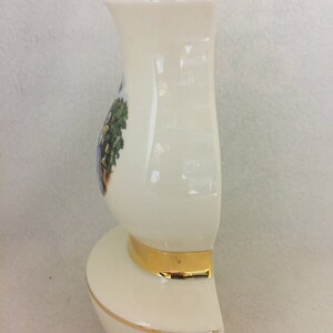 May include: A white ceramic vase with a gold rim and base. The vase has a floral design on the front.