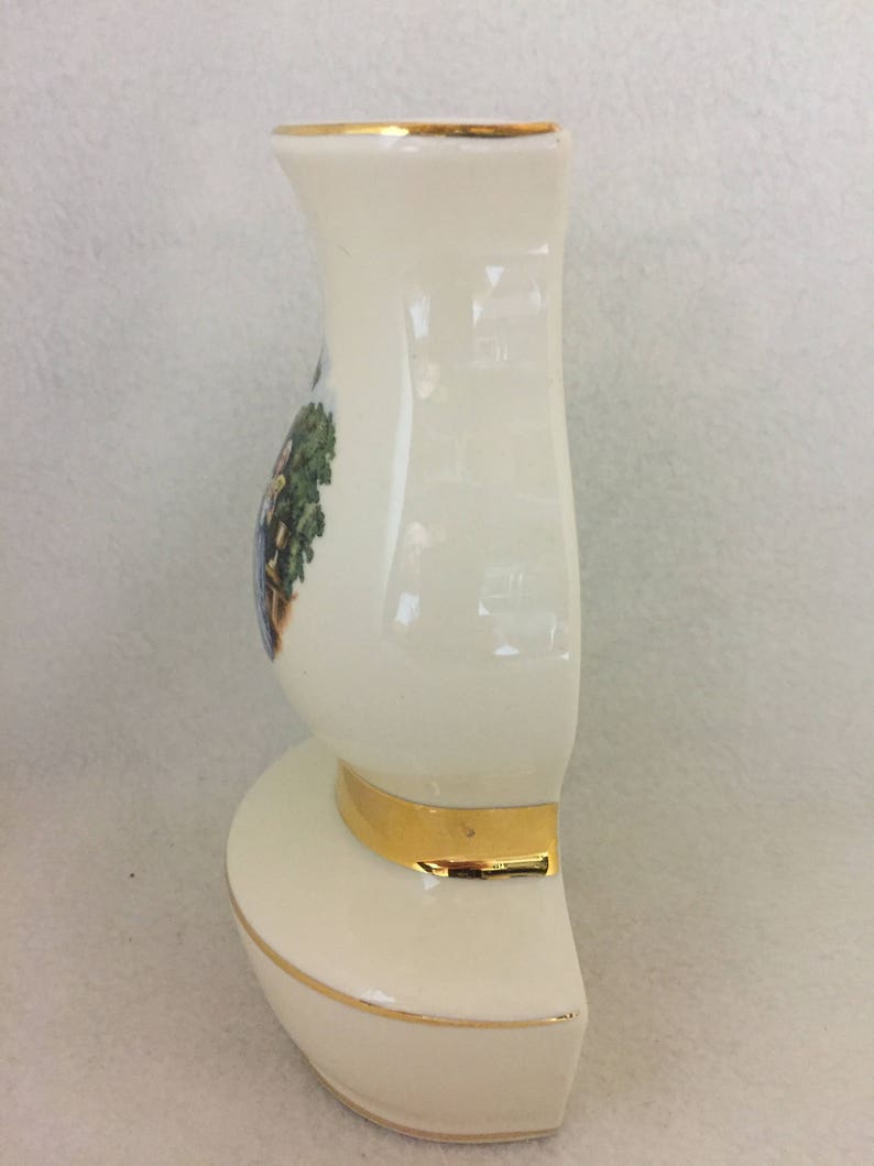 May include: A white ceramic vase with a gold rim and base. The vase has a floral design on the front.